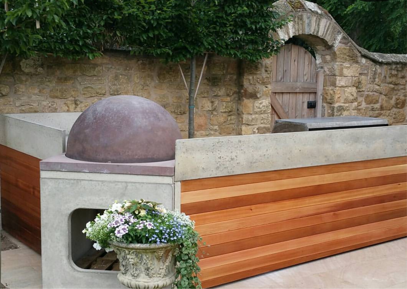 Outdoor worktop Bespoke outdoor kitchen featuring a large dome wood-fired pizza oven integrated into a concrete and cedar wood-panelled counter.