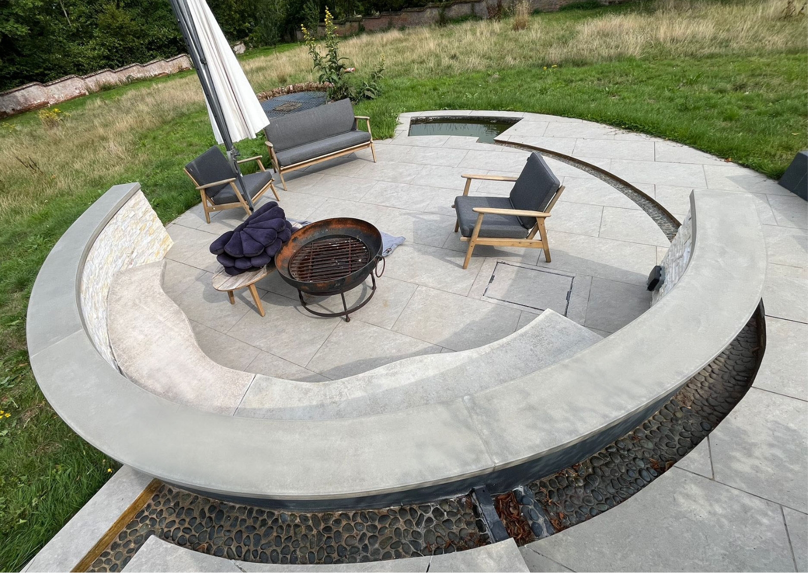 Rectangle 1225 Custom curved concrete fire pit bench integrated into a sunken circular patio with stone wall cladding and matching grey paving.
